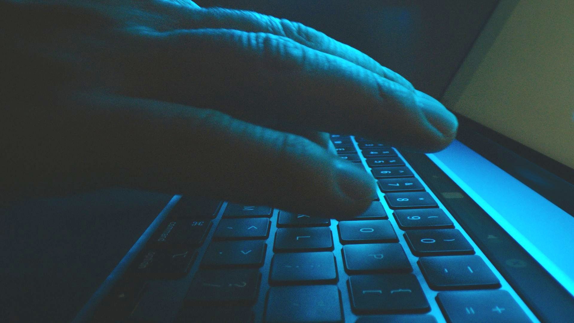 A person is typing on a laptop keyboard in the dark.