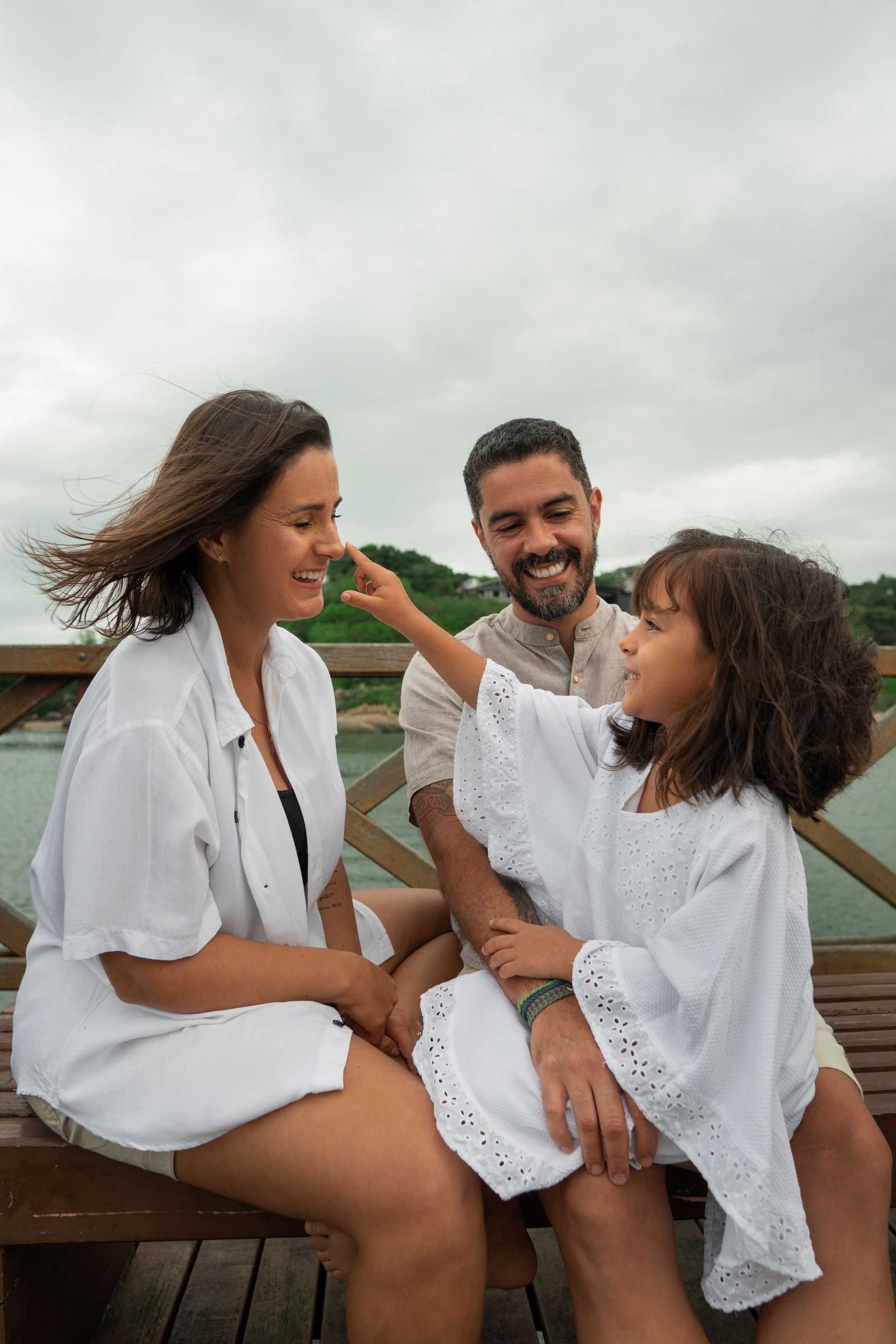 A family is sitting on a wooden bench near a body of water.