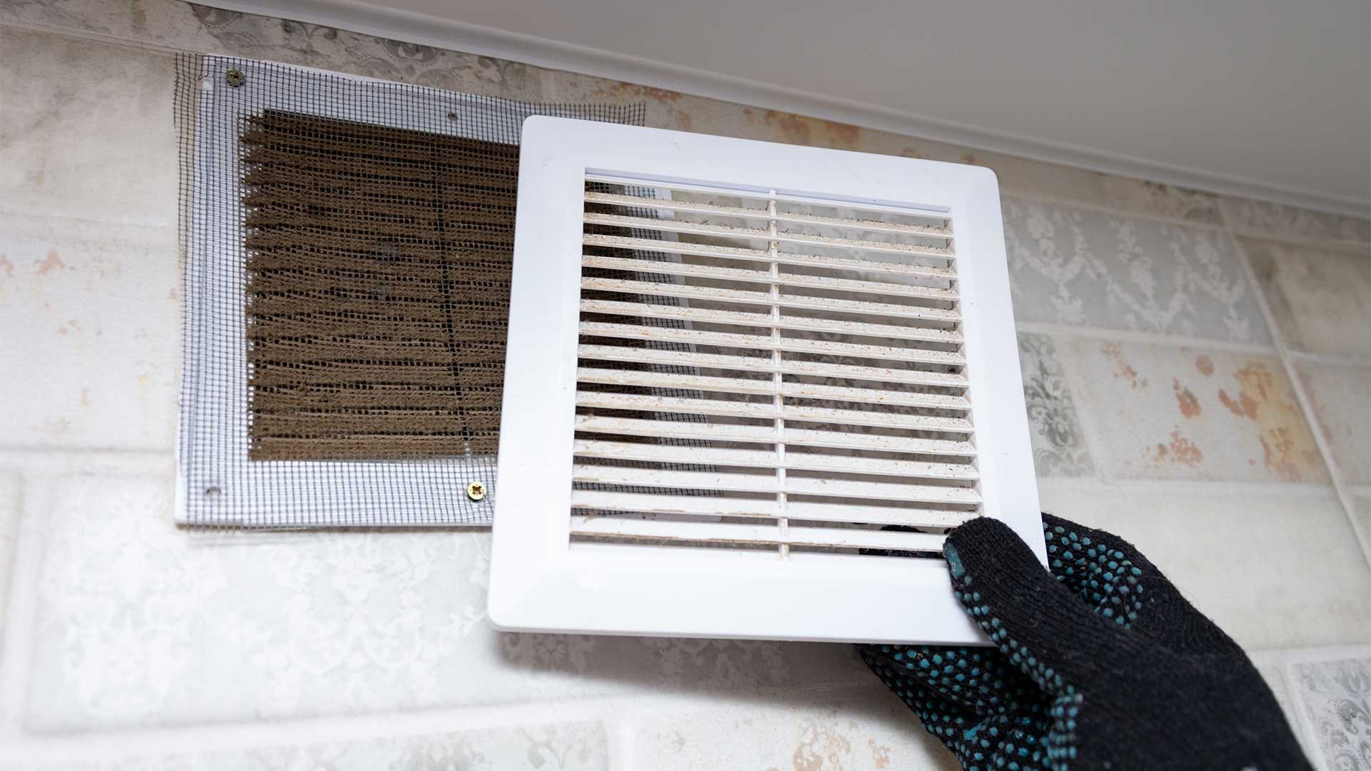 A person is holding a vent cover over a hole in the wall.