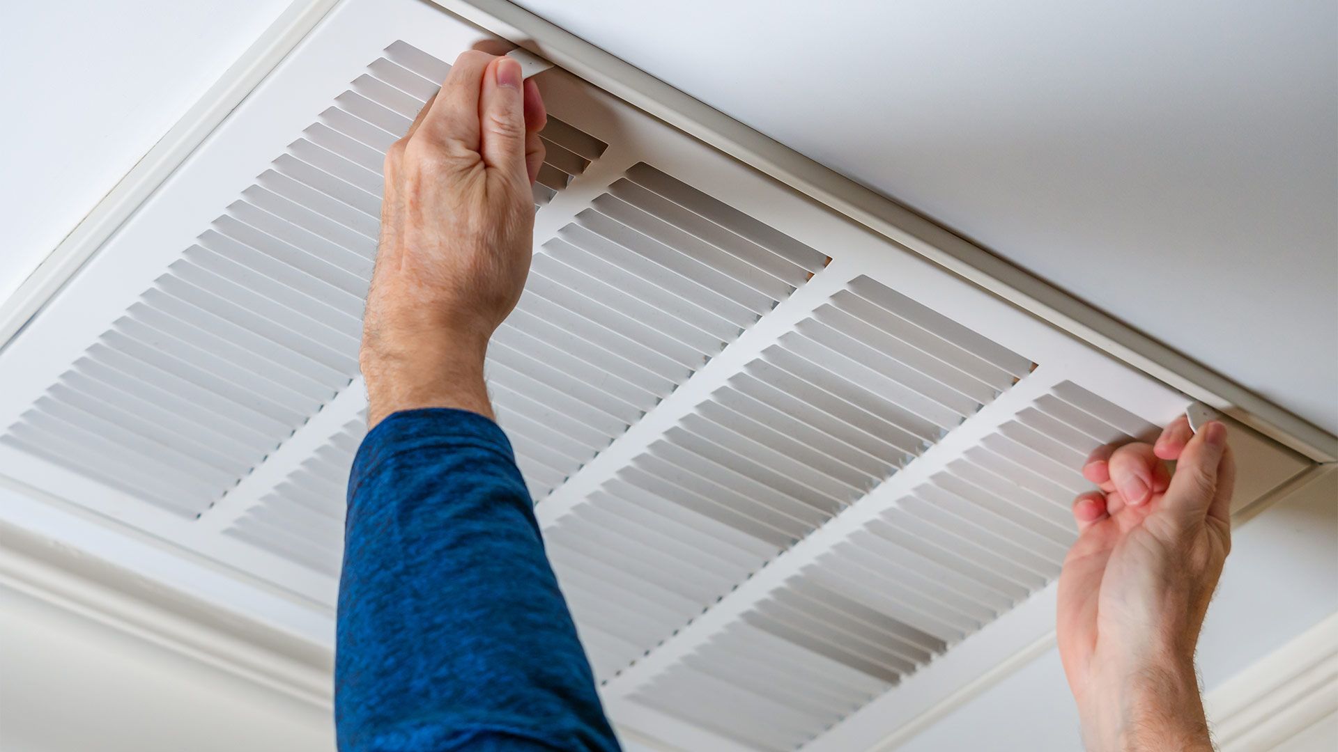 A person is cleaning an air vent on the ceiling.