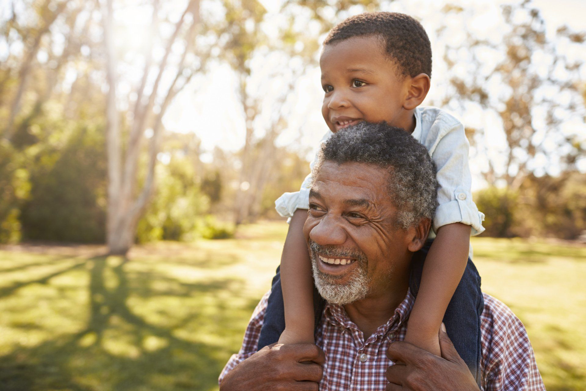 grandfather smiling with grandson on his shoulders in a park sun shining day