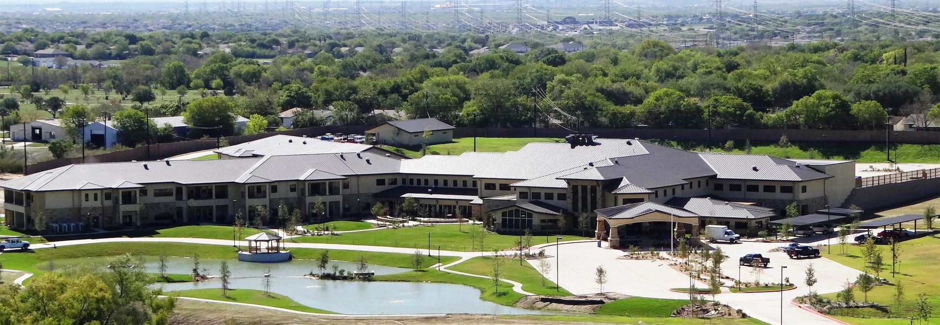 Aerial view of a large modern building complex with a green lawn and trees in a suburban area