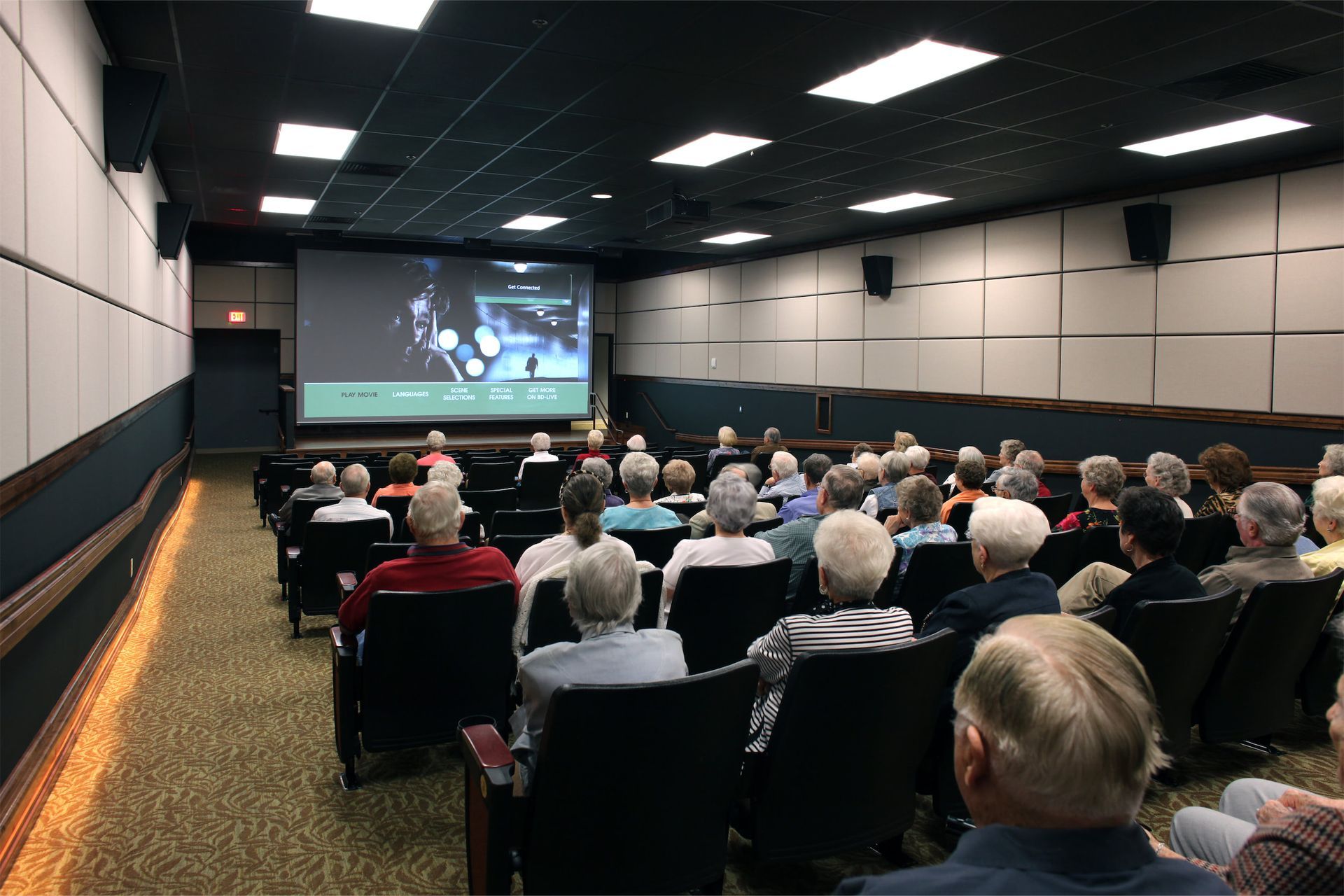 Senior care residents seated in a theater watching a movie on the screen. 