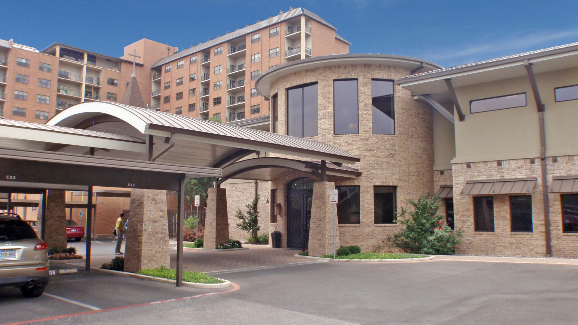 Nursing home entrance with a circular tower and a low brick building on a sunny day.