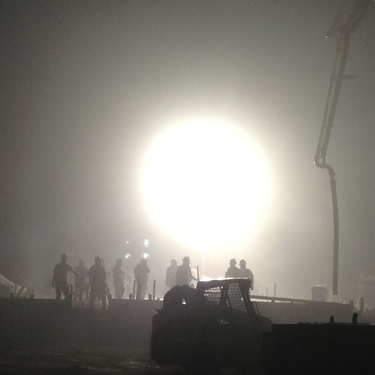 A group of people are standing in front of a large light in the fog.