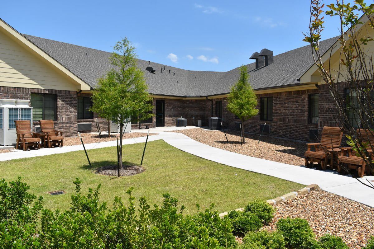 A brick senior care residence with a lawn and chairs in front of it