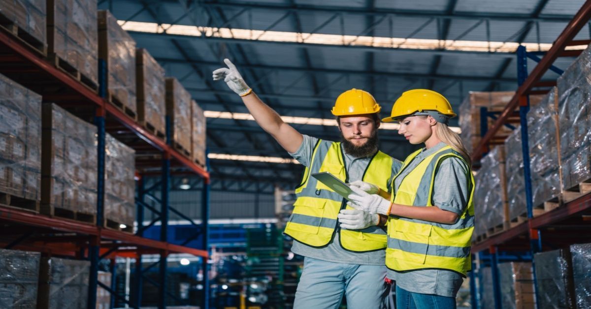 Two warehouse workers, wearing safety vests and helmets, review inventory data on a tablet, representing real-time operational visibility enabled through a successful Business Central migration.