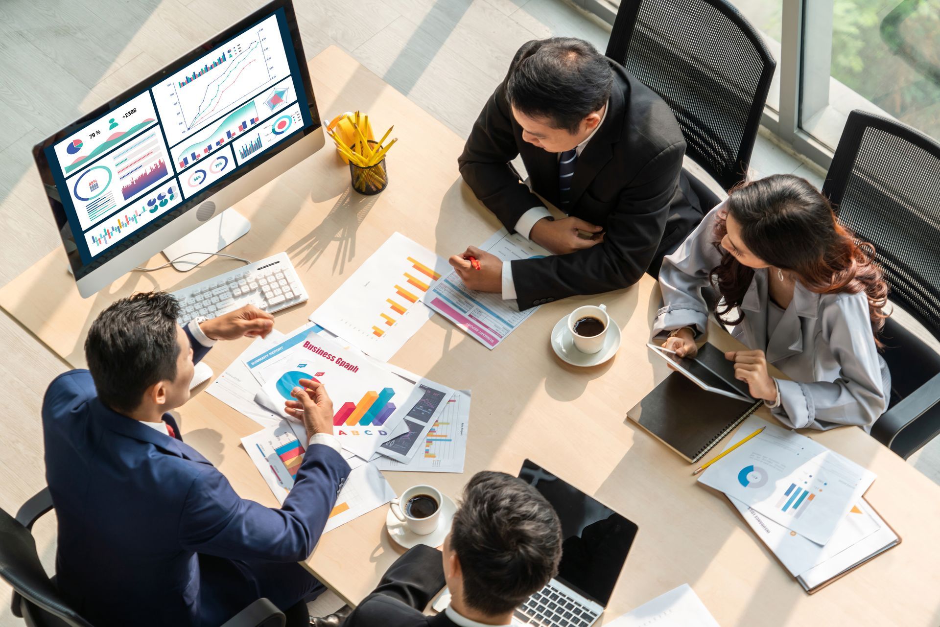 Business team in an office meeting, woman pointing at a computer screen. Others look on attentively.
