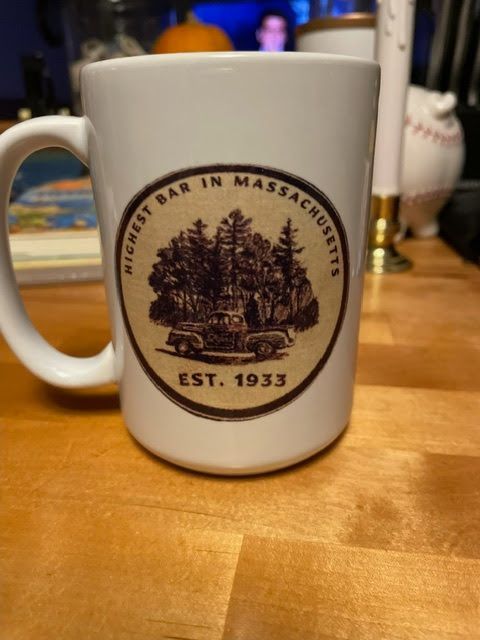 A white coffee mug featuring a brown circular logo that says 