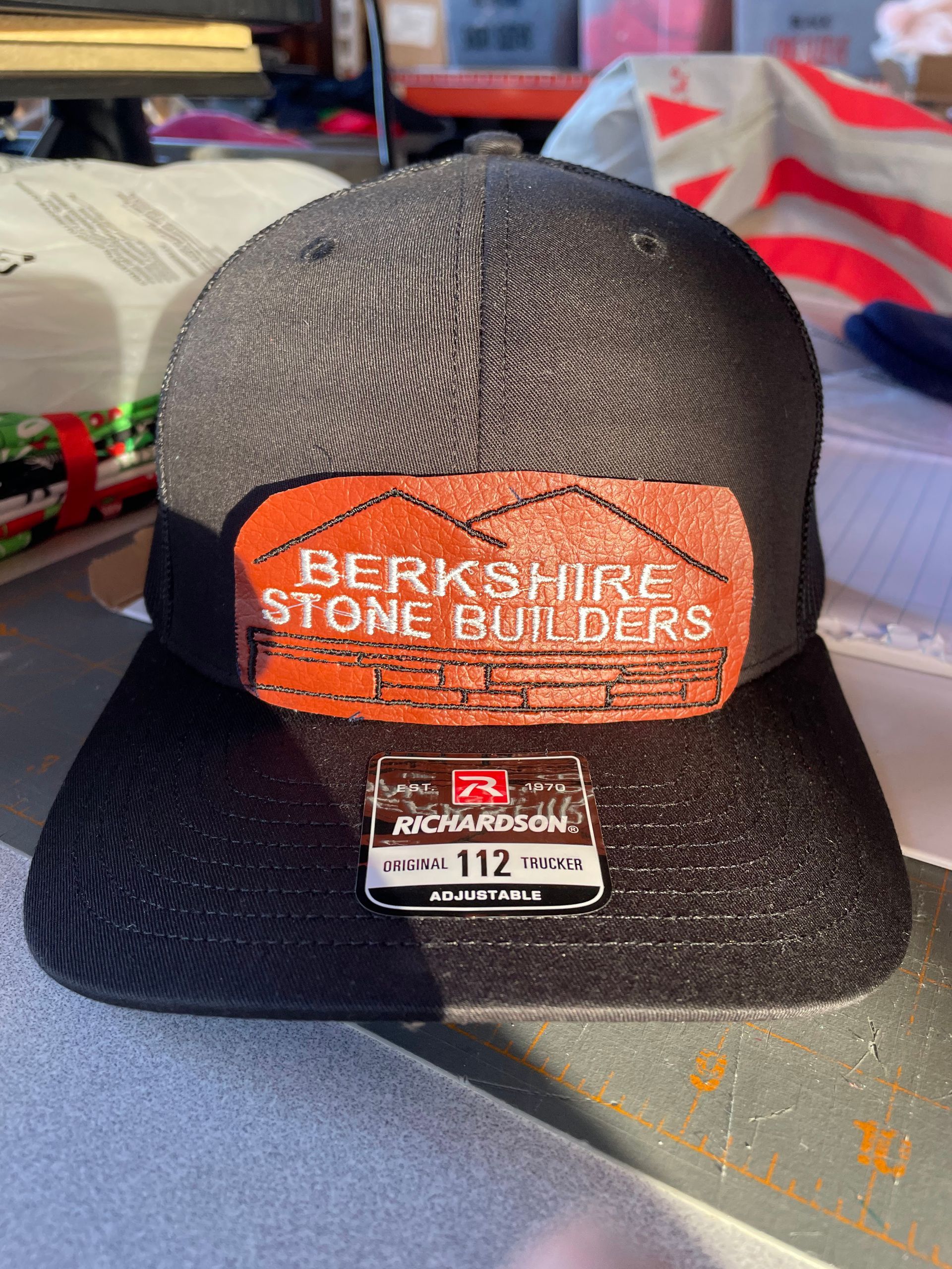A black Richardson 112 trucker hat with a copper-colored patch that says 