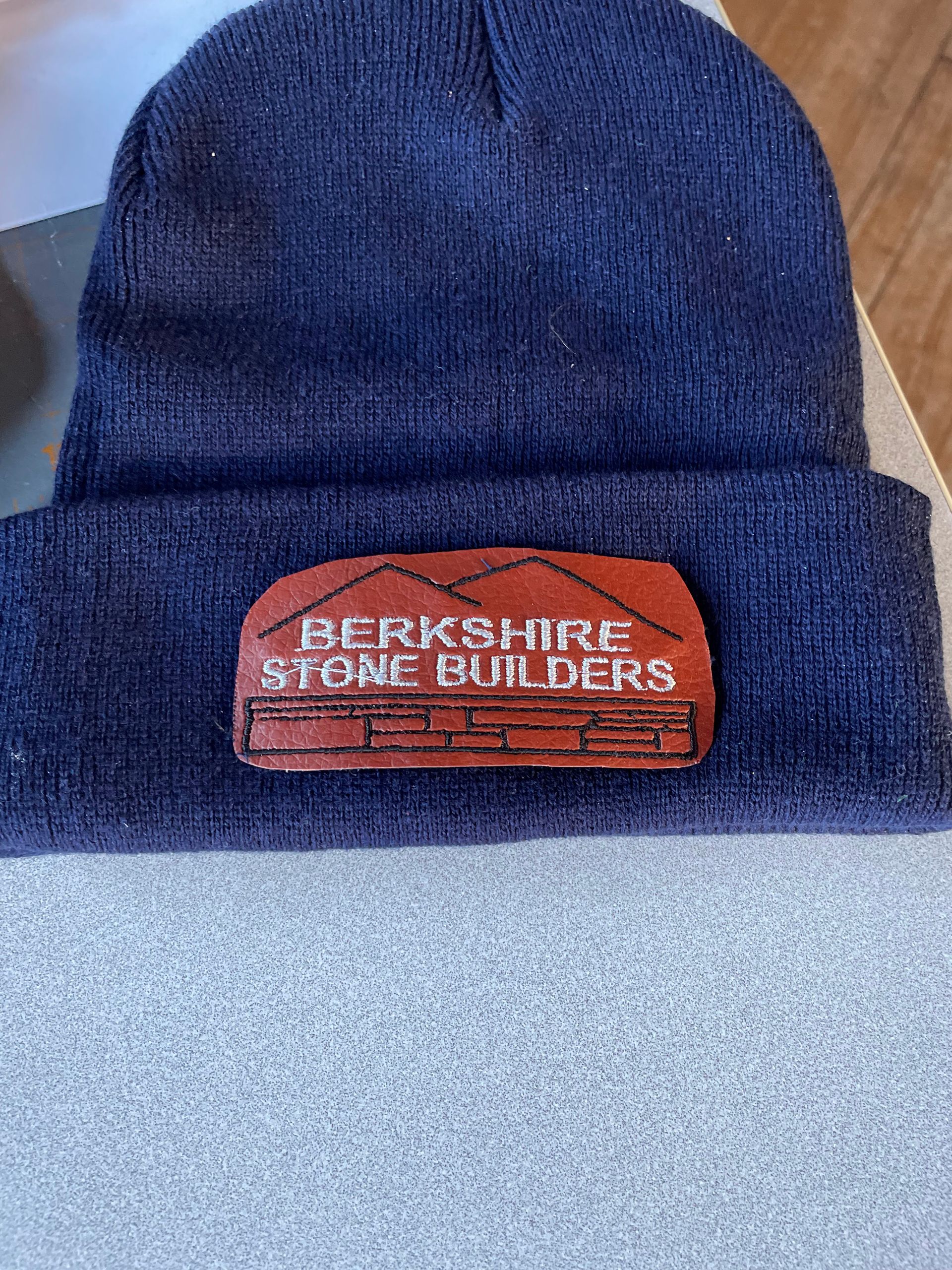 A dark blue knit beanie with a brown leather patch featuring the text 