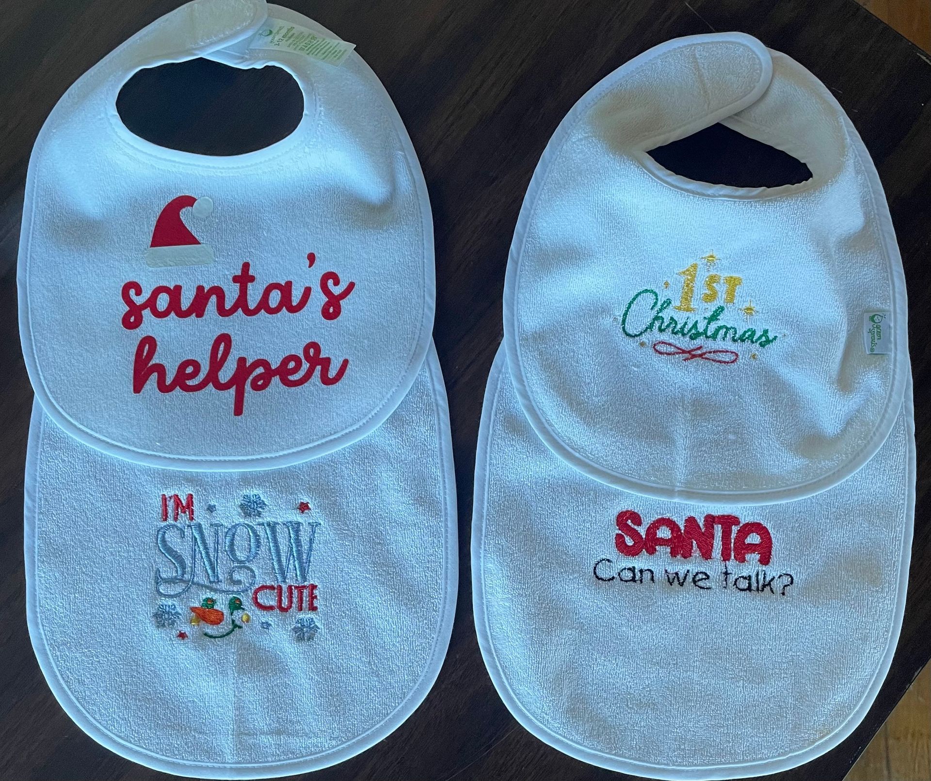 Four white baby bibs with holiday-themed embroidery, including phrases like 