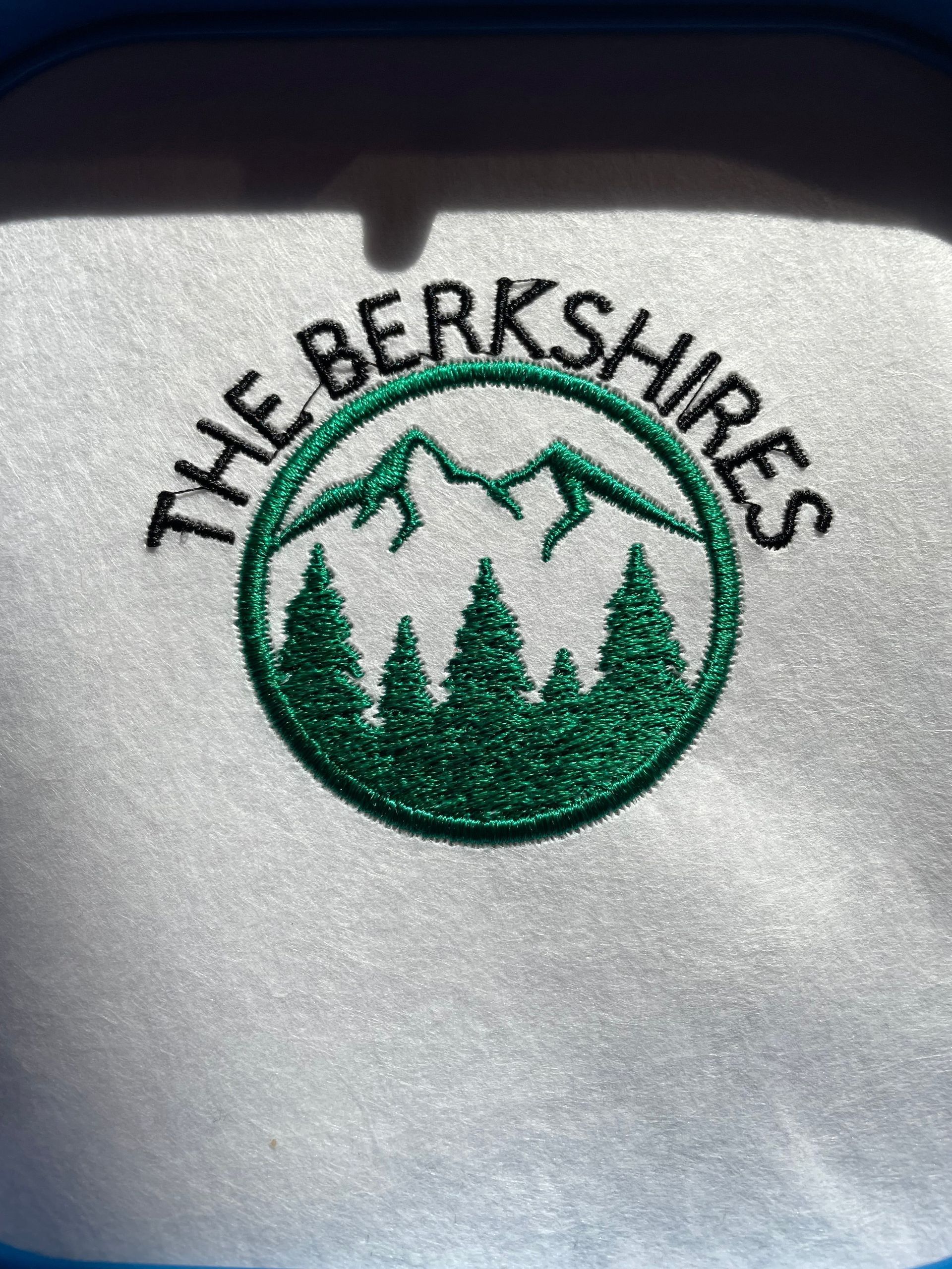 An embroidered patch featuring green pine trees and mountain peaks inside a circle with the text 