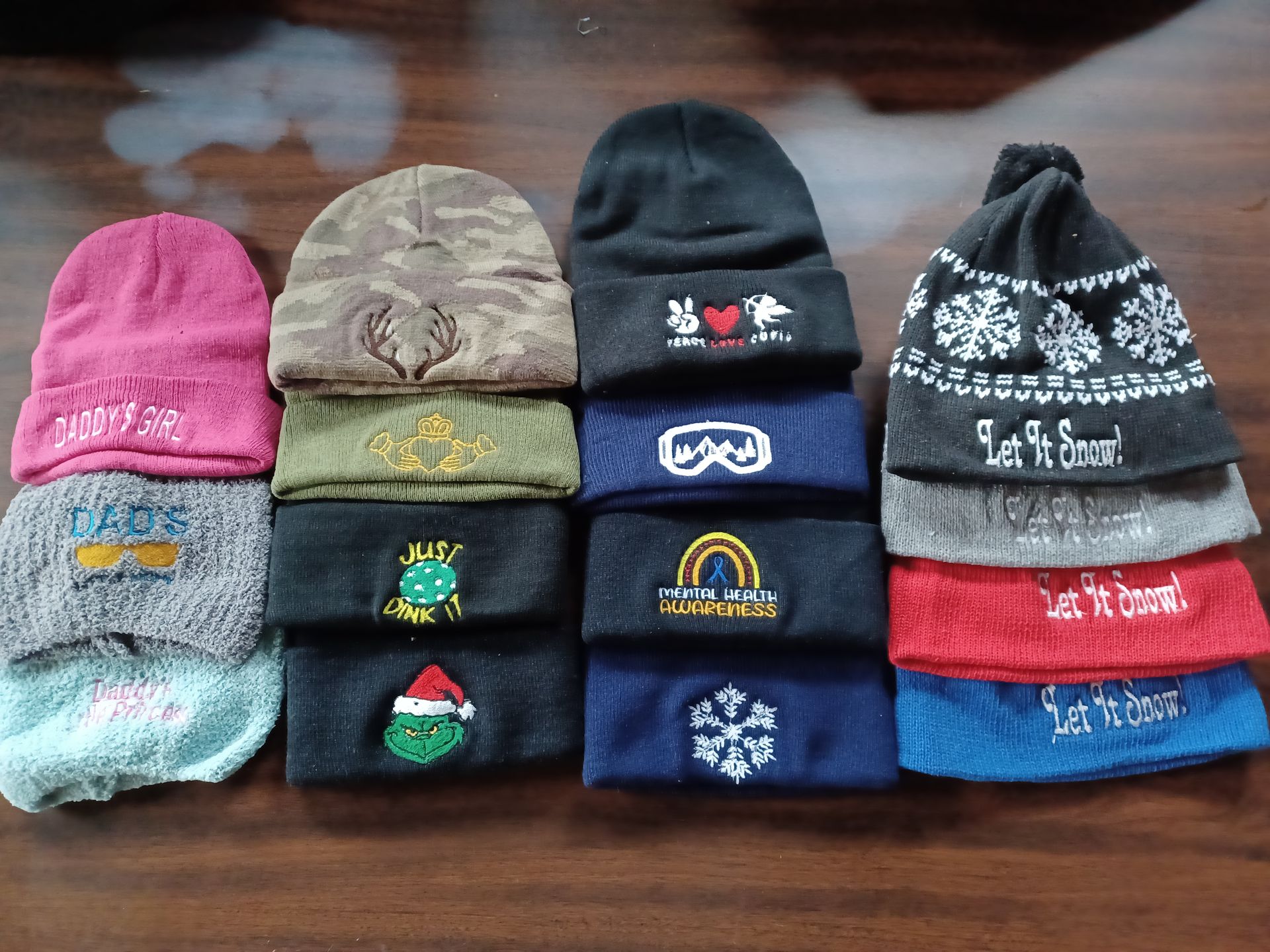 Four stacks of folded knit winter hats with various patterns and colors arranged on a wooden table.