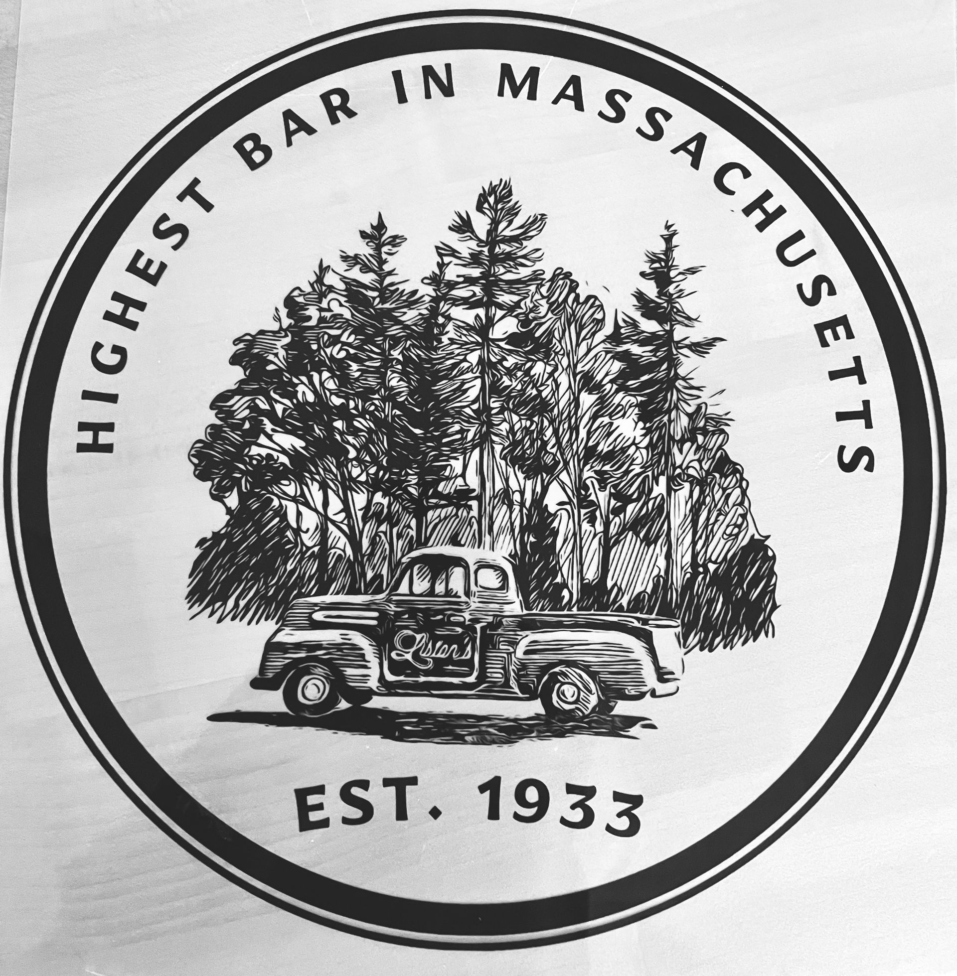 A black-and-white circular logo featuring a vintage pickup truck in front of a forest, labeled 