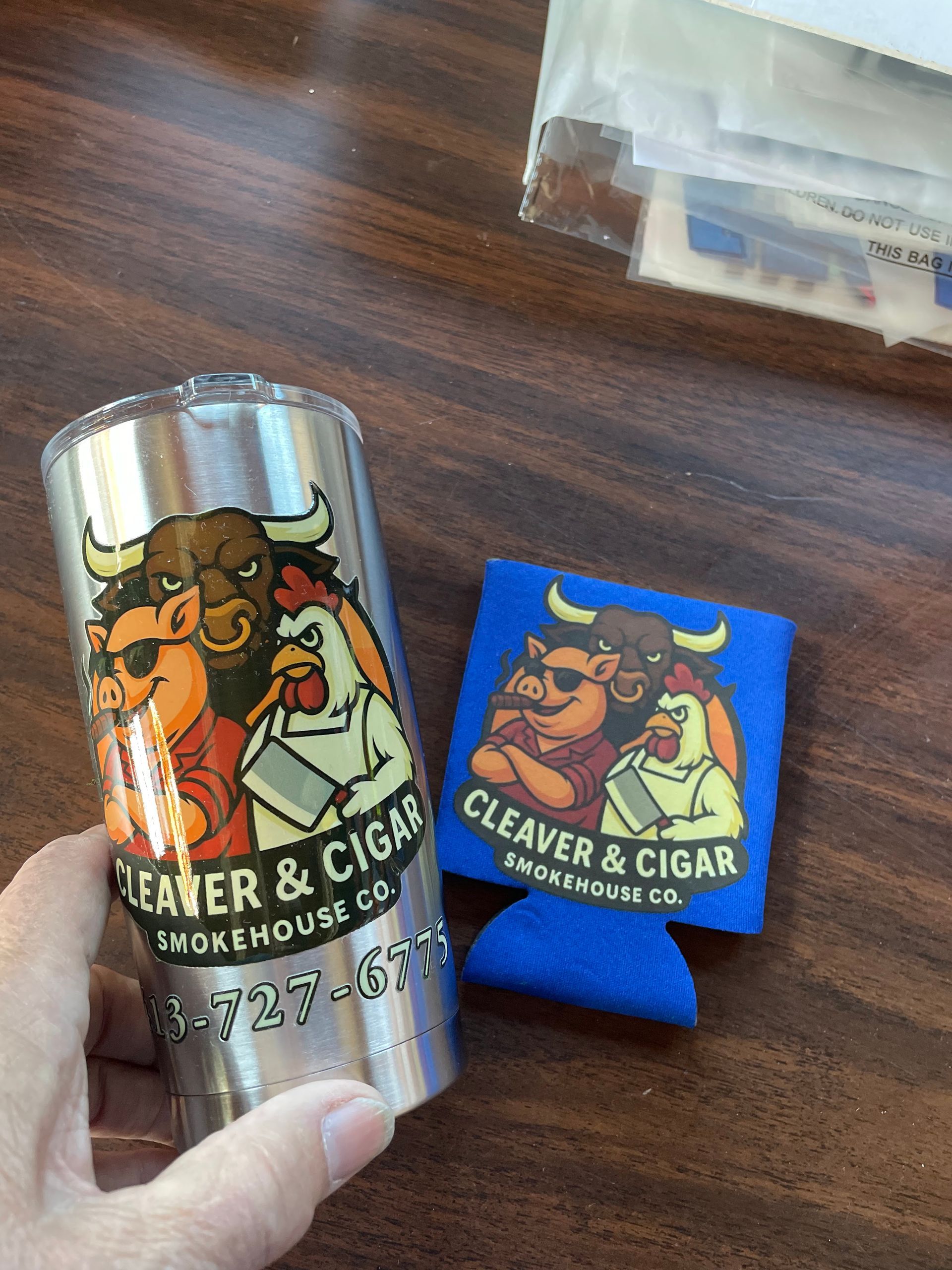 A silver tumbler and a blue foam koozie, both branded with the 