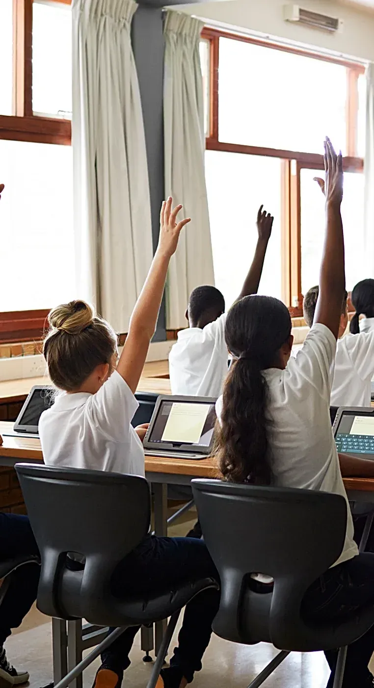 A group of children are raising their hands in a classroom.