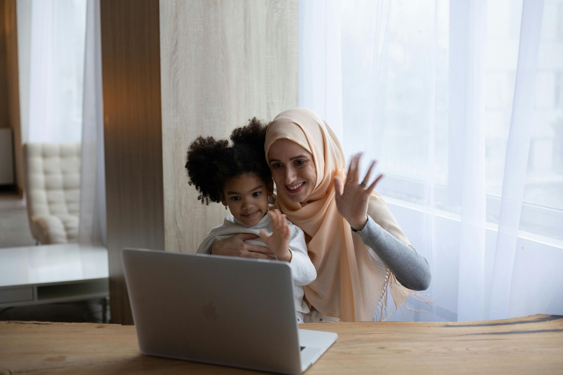 Woman and young gir waving in front of computer.