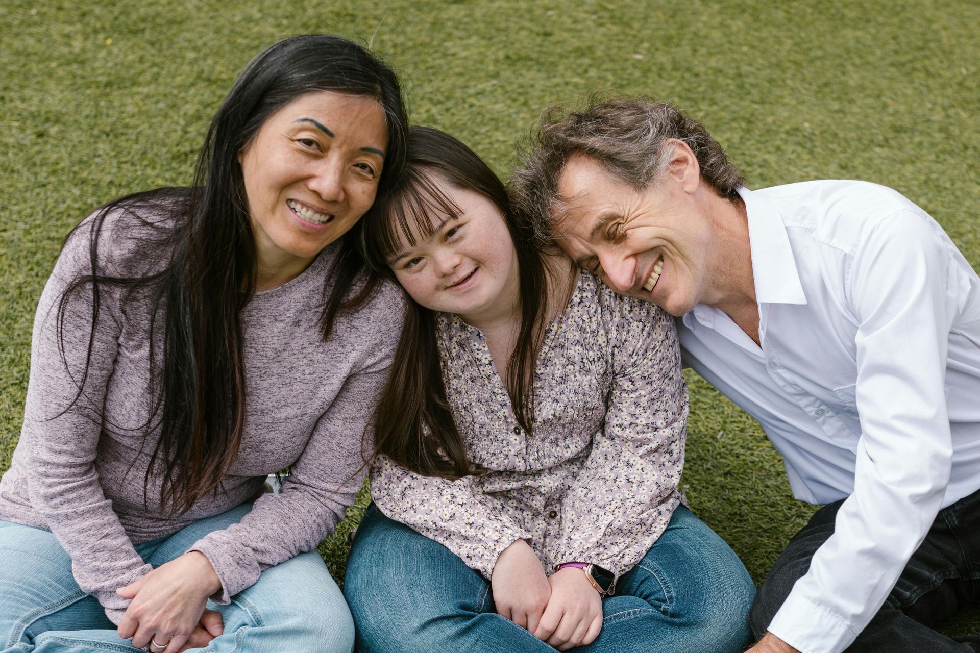 A family with a girl with down syndrome is sitting on the grass together.