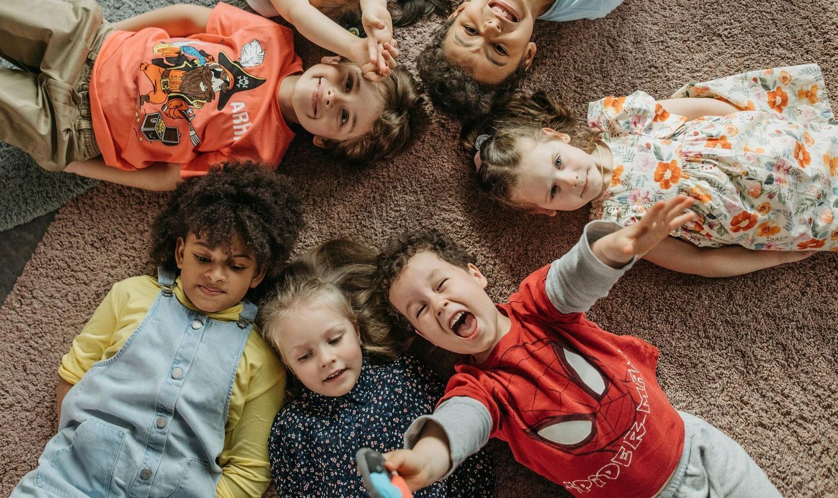 Children laying on ground on carpet, in a circle.