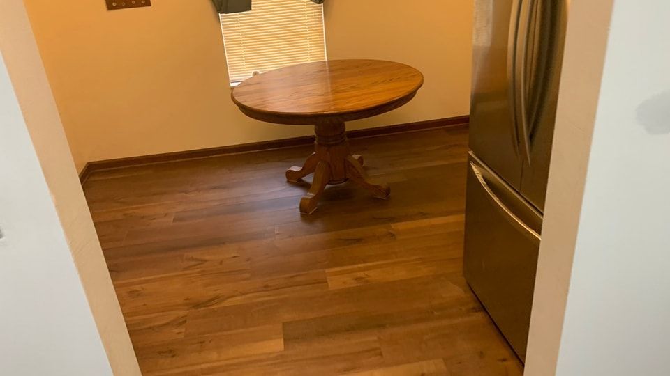 A small wooden table is sitting in a kitchen next to a refrigerator.