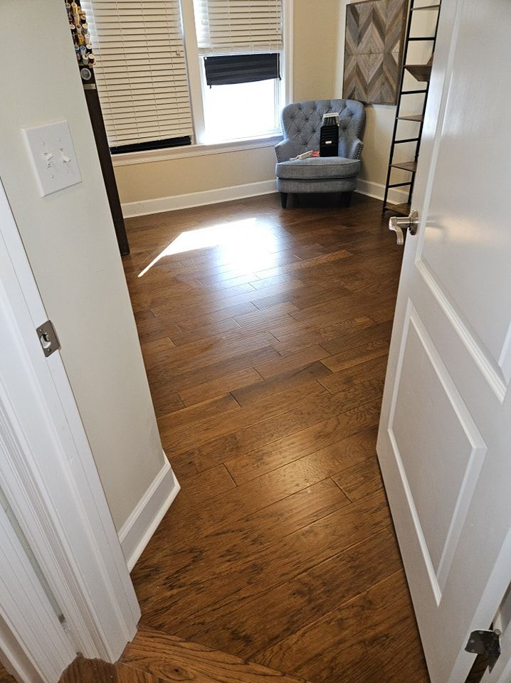 A hallway with hardwood floors leading to a living room with a chair and stairs.