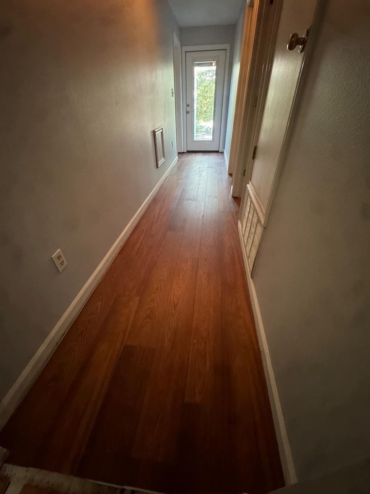 A long hallway with hardwood floors and a door.