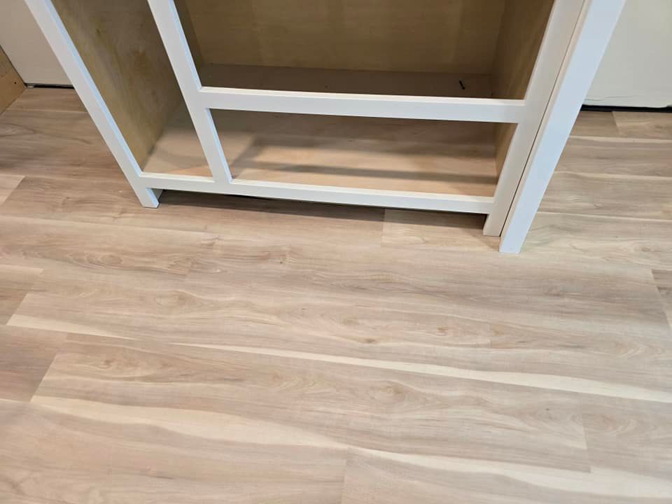A white cabinet is sitting on a wooden floor next to a wooden shelf.