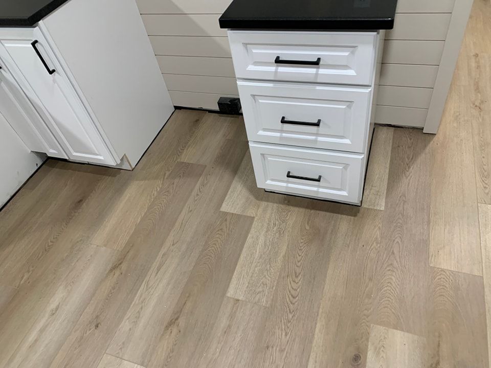 A white cabinet with three drawers is sitting on a wooden floor in a kitchen.