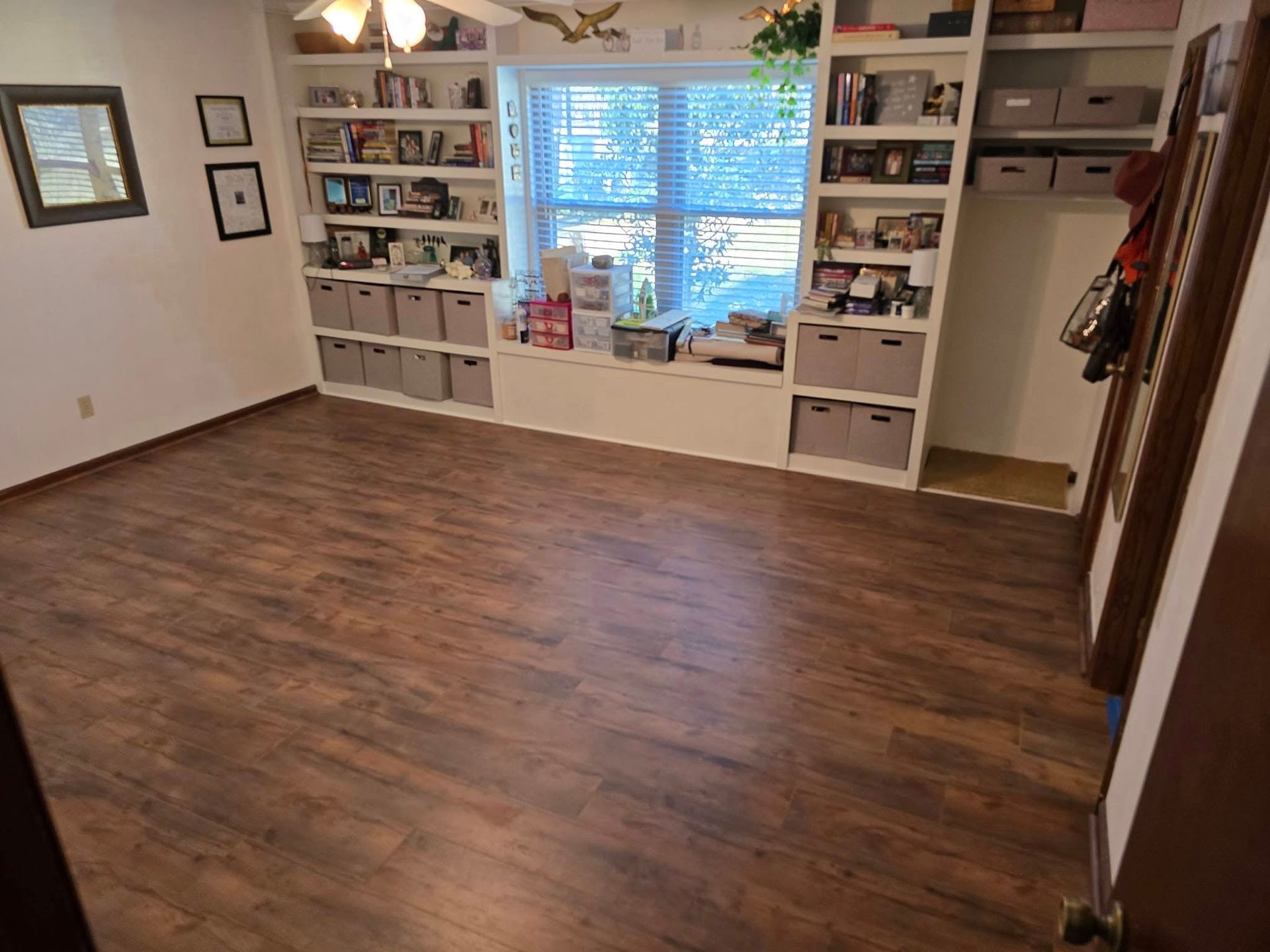 A living room with hardwood floors , shelves , a window and a ceiling fan.