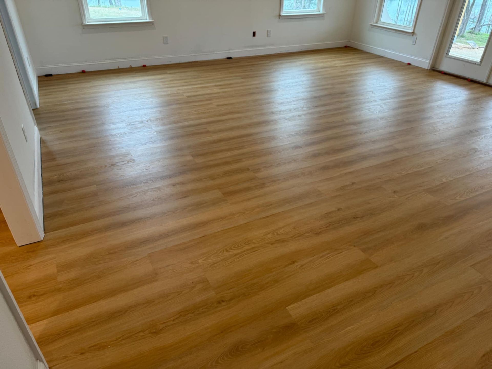 A living room with a wooden floor and two windows.