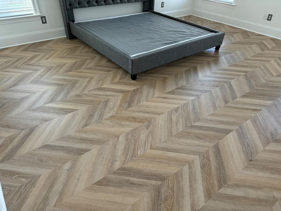 A bedroom with a bed and a wooden floor with a herringbone pattern.