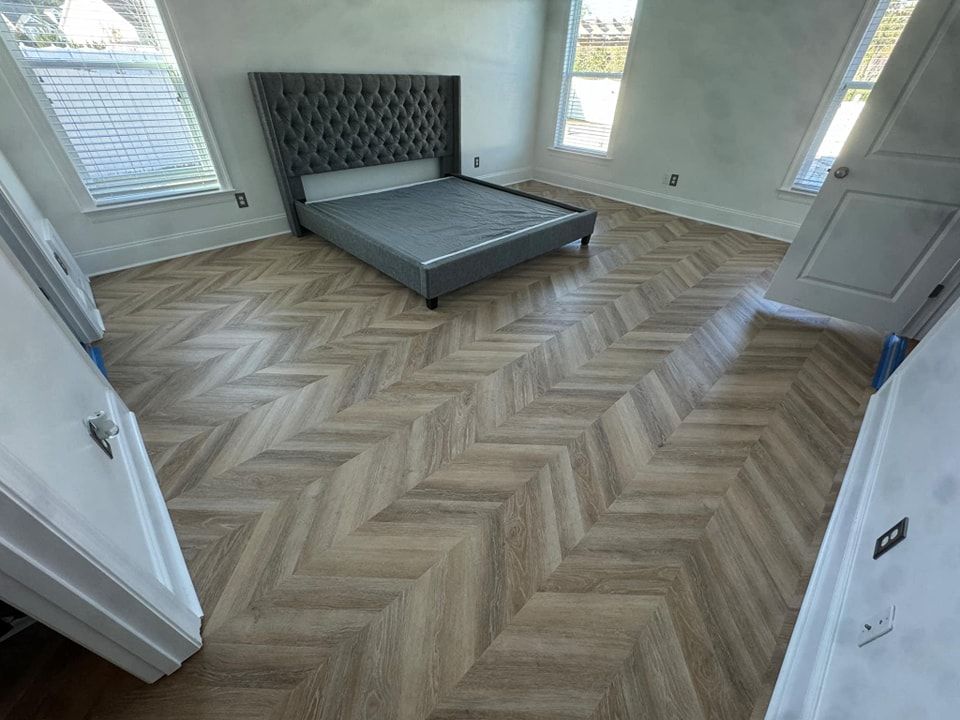 A bedroom with a bed and a herringbone floor.