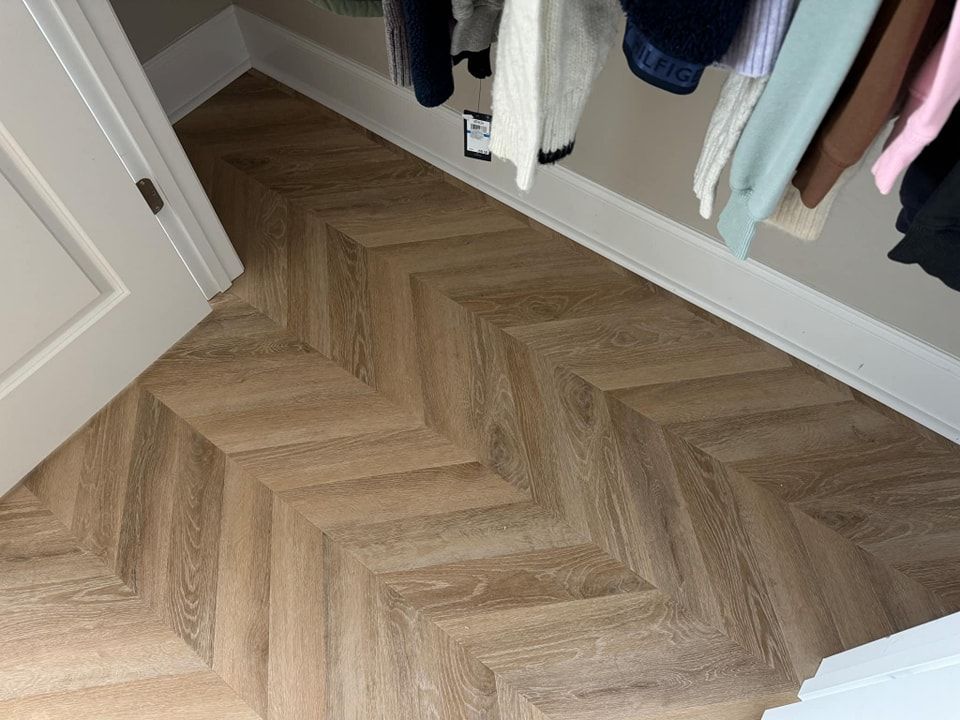 A closet with a wooden floor and clothes hanging on the wall.