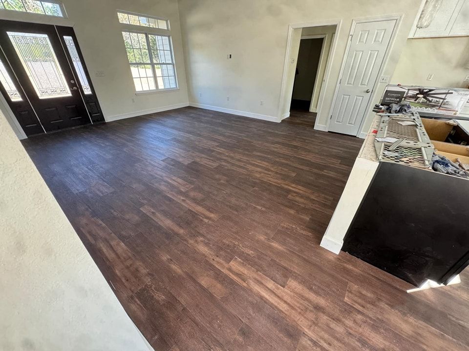 A living room with hardwood floors and a kitchen in the background.