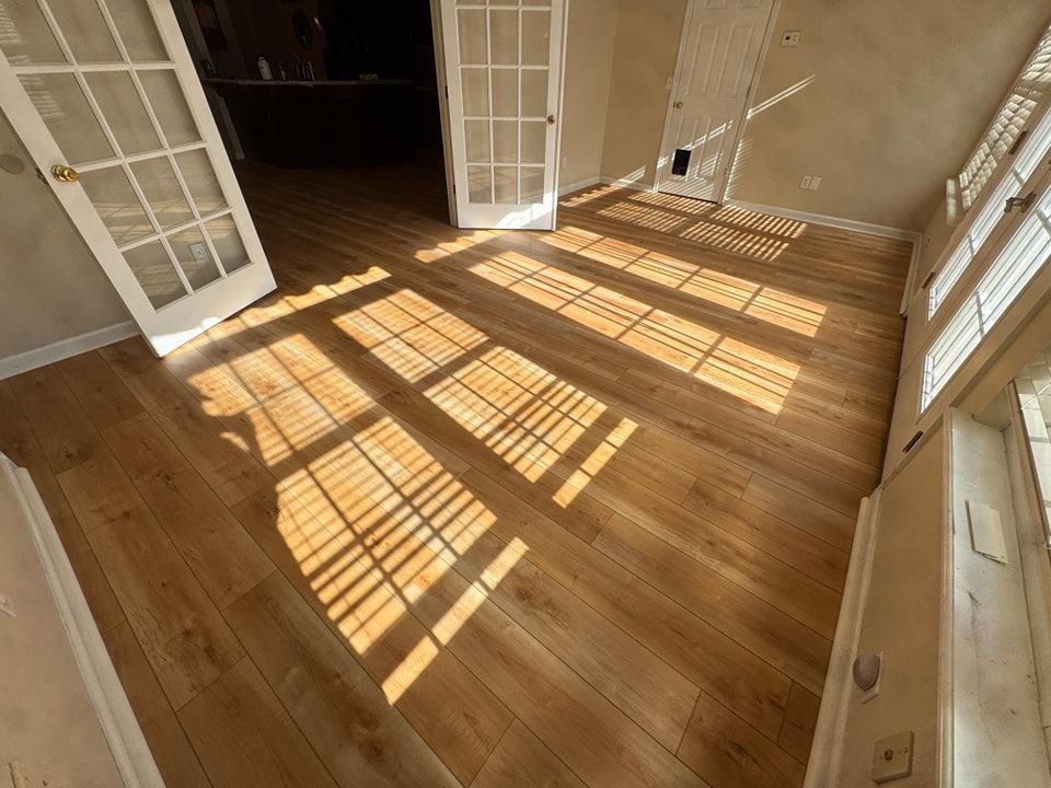 The sun is shining through the windows on the wooden floor of a room.