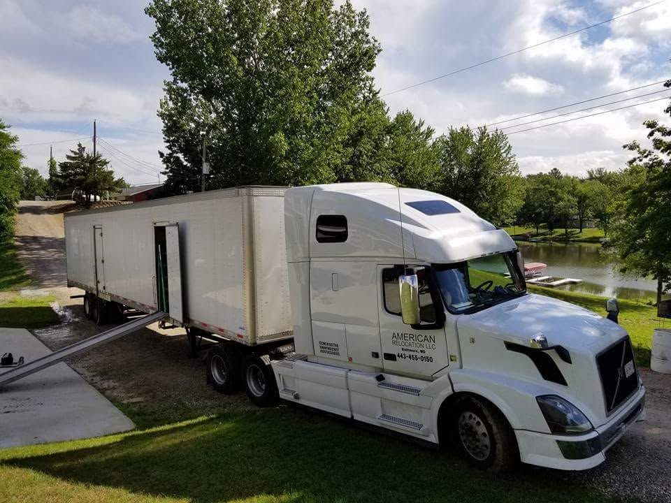 White semi-truck with trailer parked on a driveway, likely for moving. The truck is beside a lake.