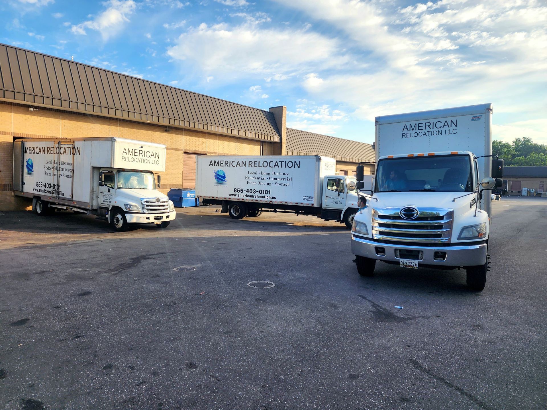 Three white American Relocation moving trucks parked in front of a brick building on a paved lot