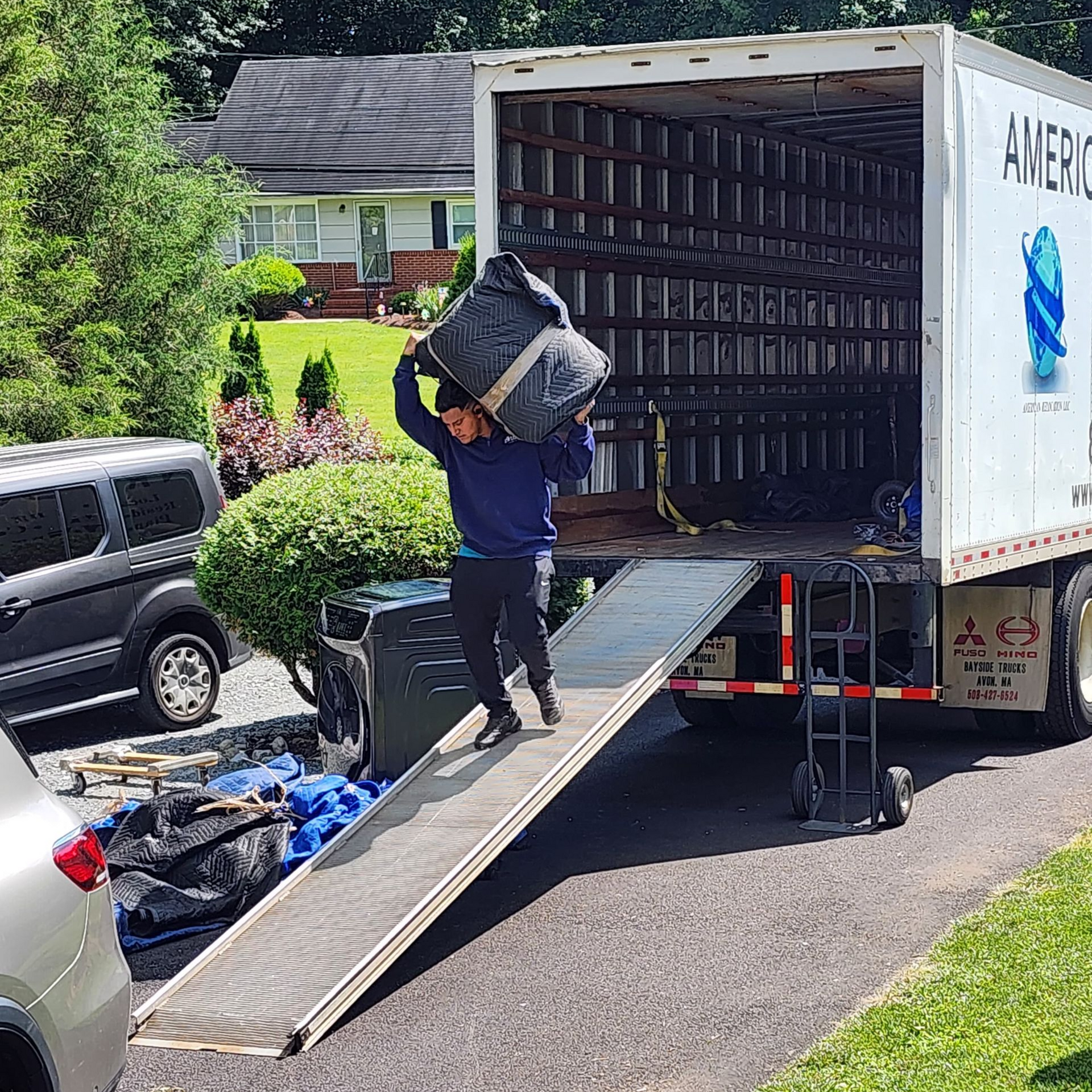 A person in a U.S. military uniform holds a small model house in their hands in front of an American flag.
