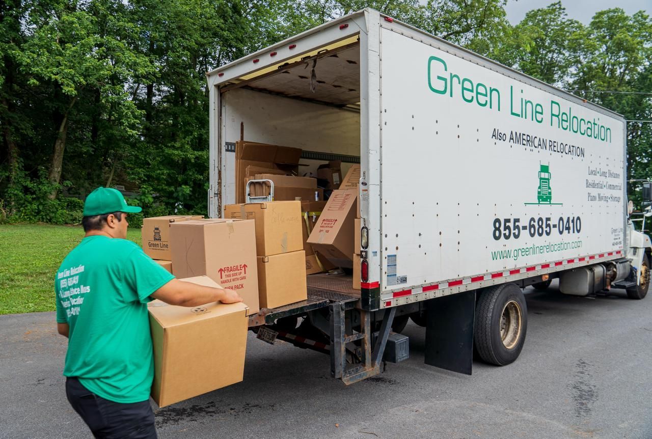 A mover loads a cardboard box into a Green Line Relocation truck.