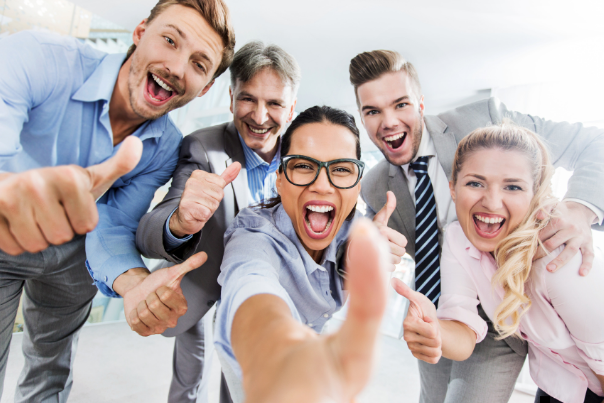 A diverse group of enthusiastic business professionals in an office setting, smiling and giving thum