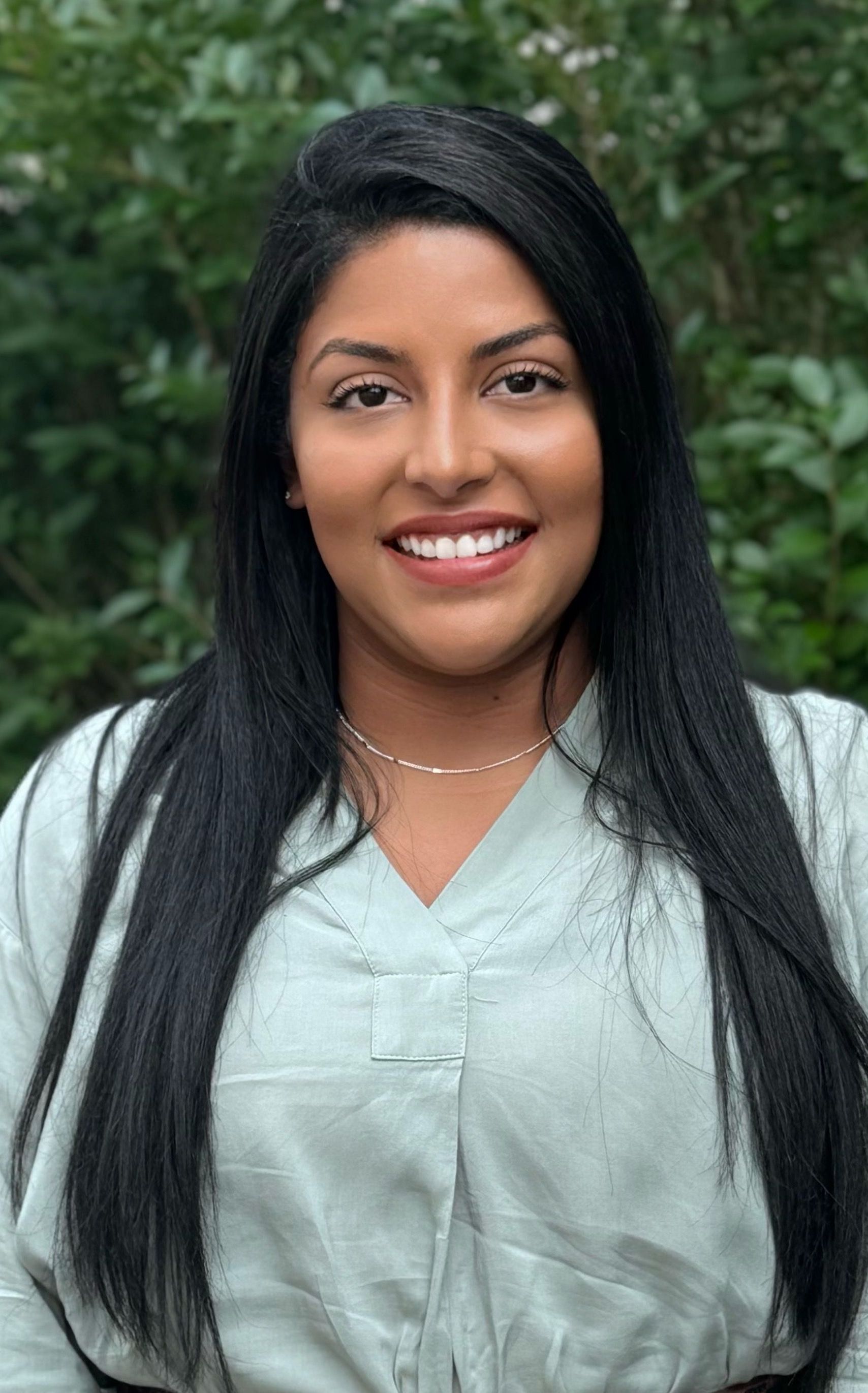A woman is sitting at a desk with a laptop and a vase of flowers.