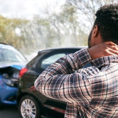 a man in a plaid shirt is holding his neck in front of a car accident .