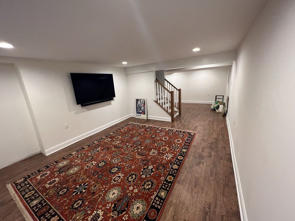 A basement with a rug and a flat screen tv on the wall.