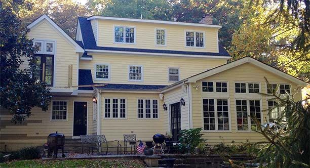A large yellow house with a black roof is surrounded by trees