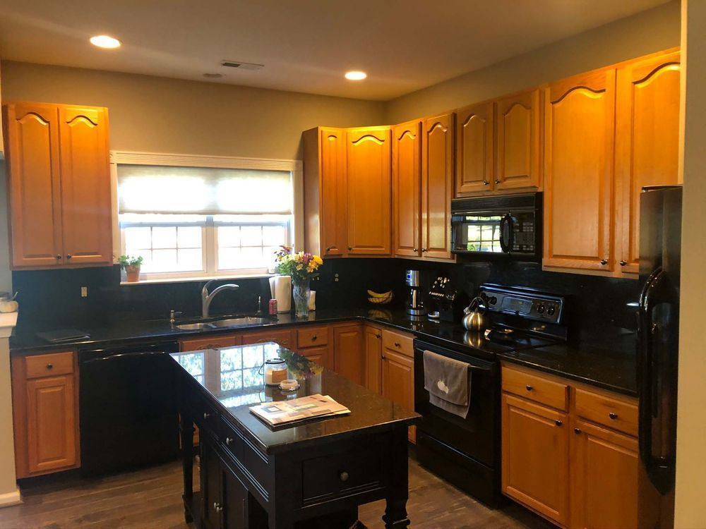 A kitchen with wooden cabinets , black counter tops , stainless steel appliances and a large island.