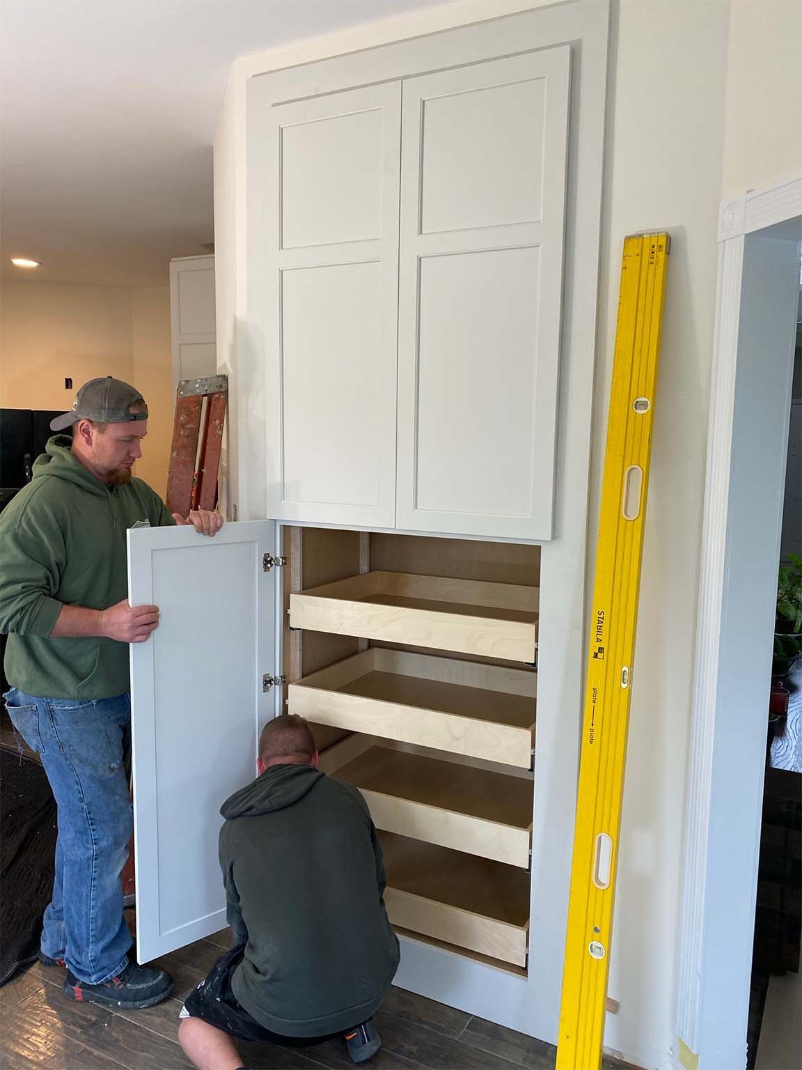 Two men are working on a cabinet in a kitchen.