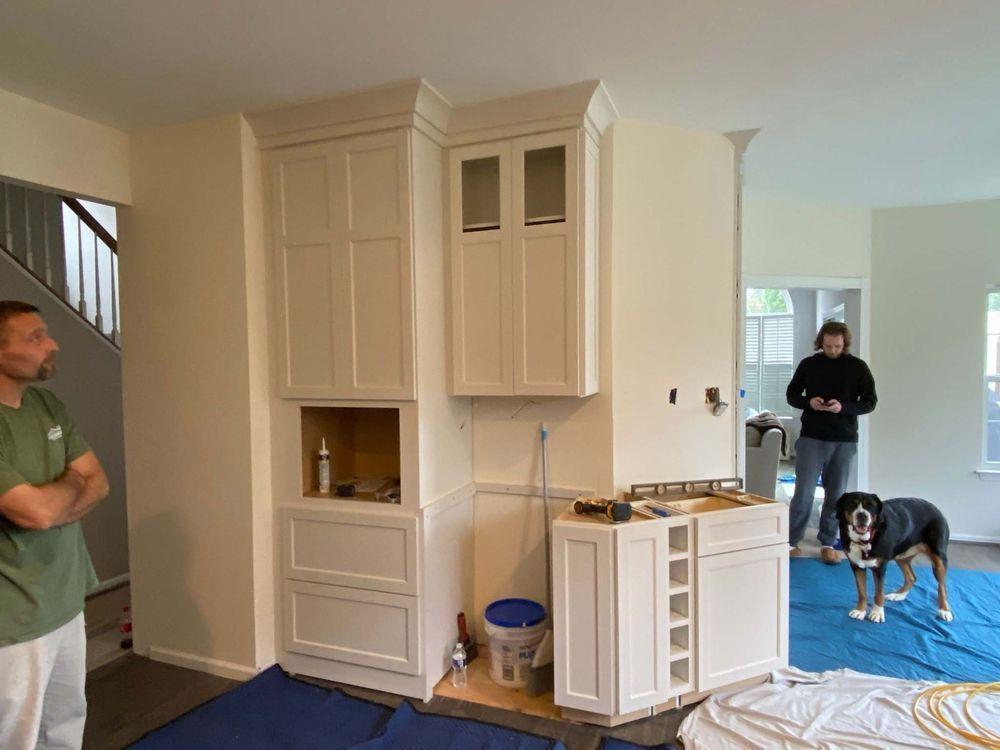 A man and a dog are standing in a room with white cabinets.