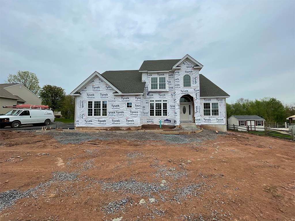 A large white house is being built in a dirt field.
