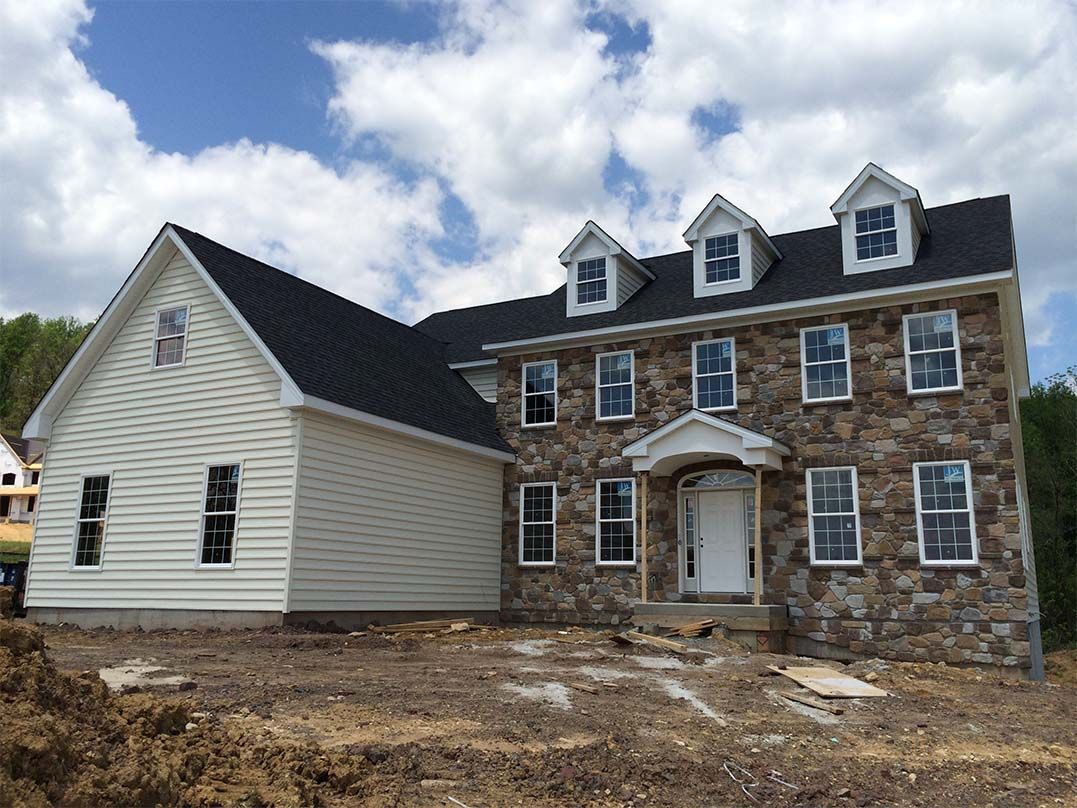 A large stone house with a white siding and a black roof